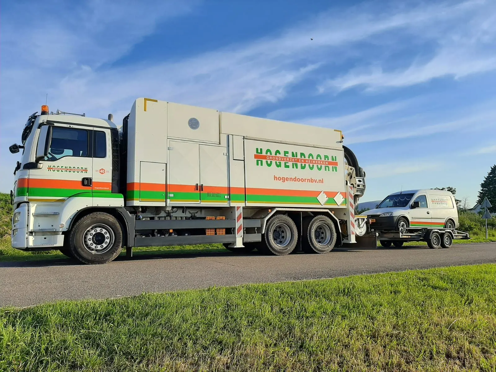 MAN grondzuigauto met aanhanger langs een dijkweg