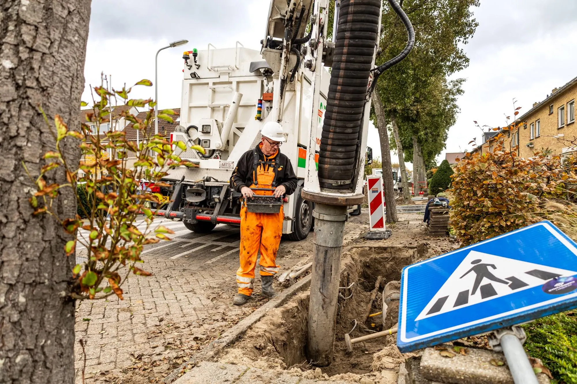 Grondzuigauto in een woonwijk, machinist met afstandsbediening, zuigslang in een sleuf met kabels