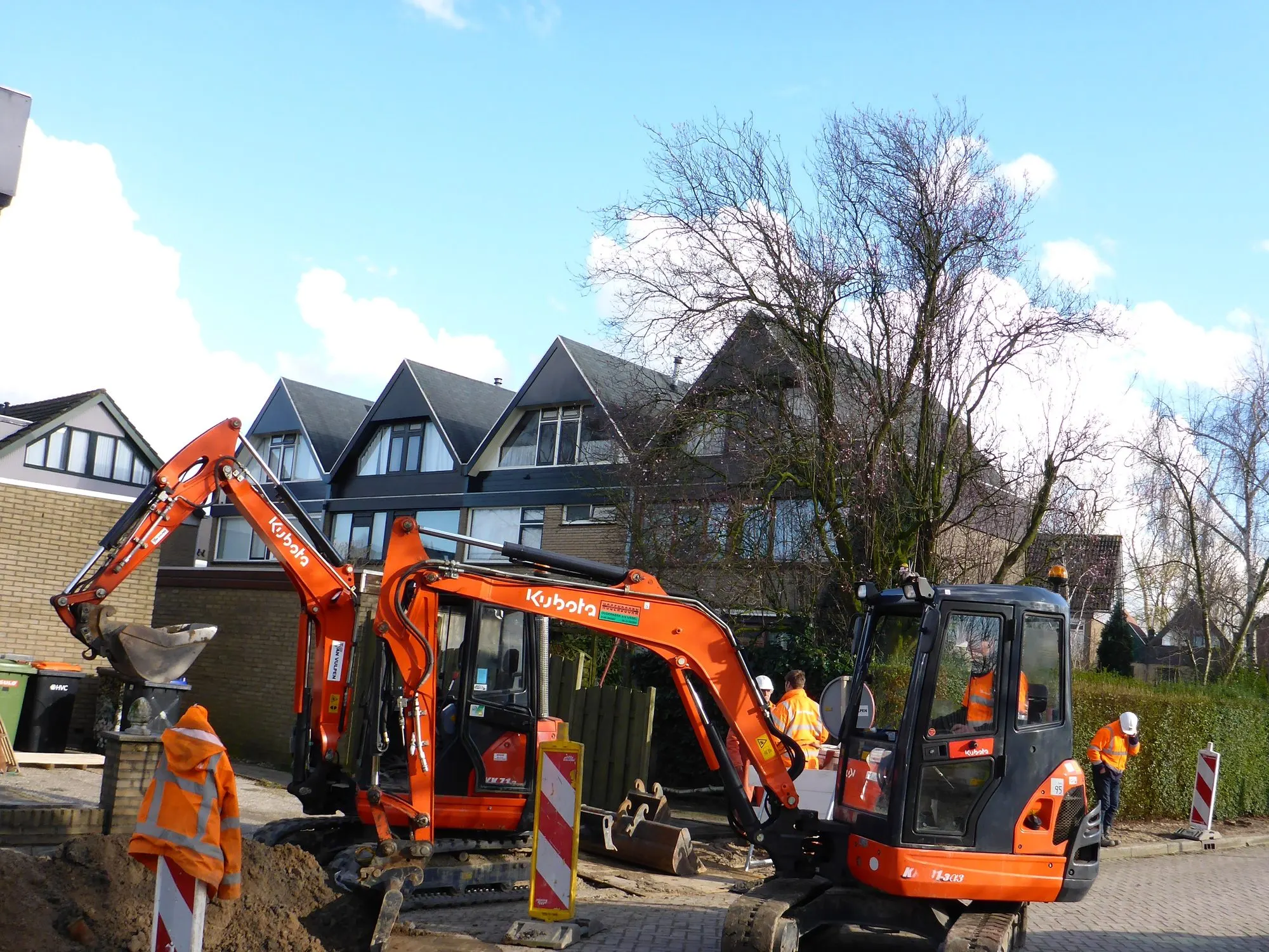 Twee Kubota minigravers graven een sleuf in een woonwijk