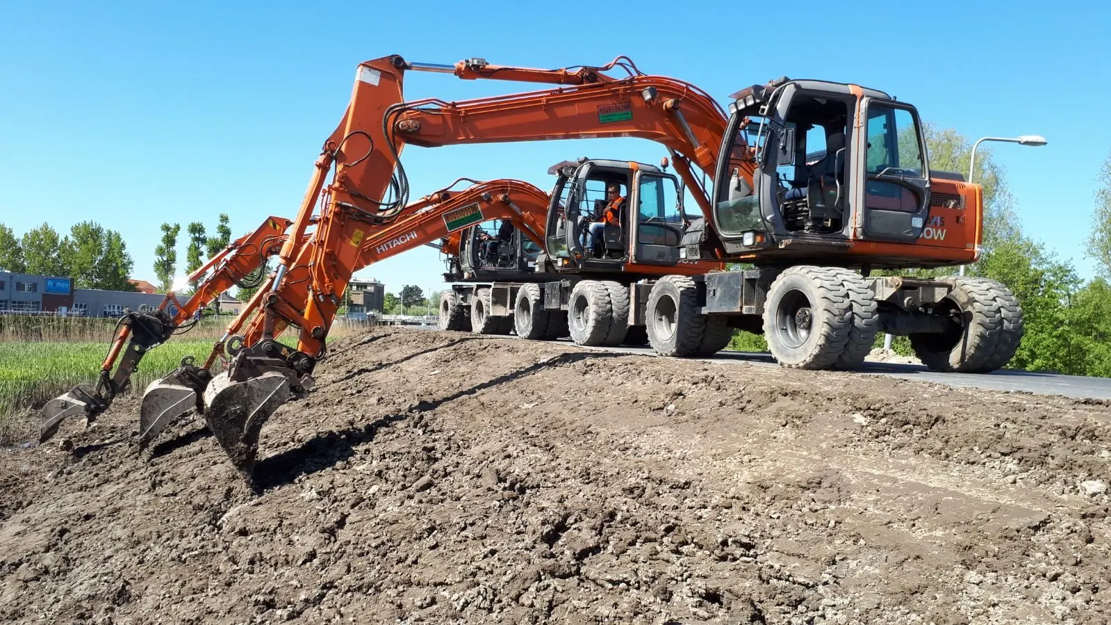 Drie oranje Hitachi mobiele graafmachines naast elkaar op een zandwal