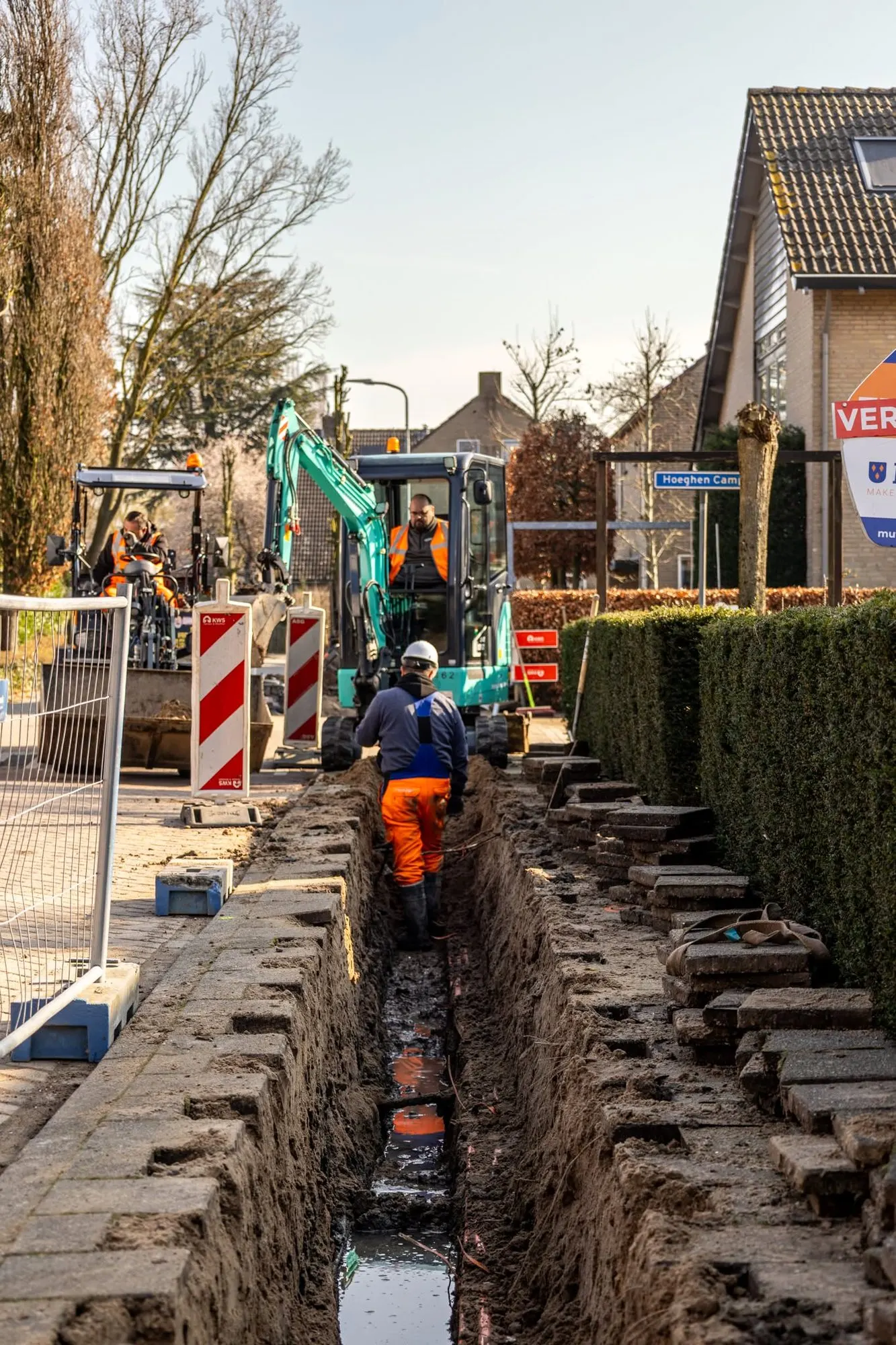 Elektrische minigraver in een sleuf in een woonwijk, grondwerker in de sleuf