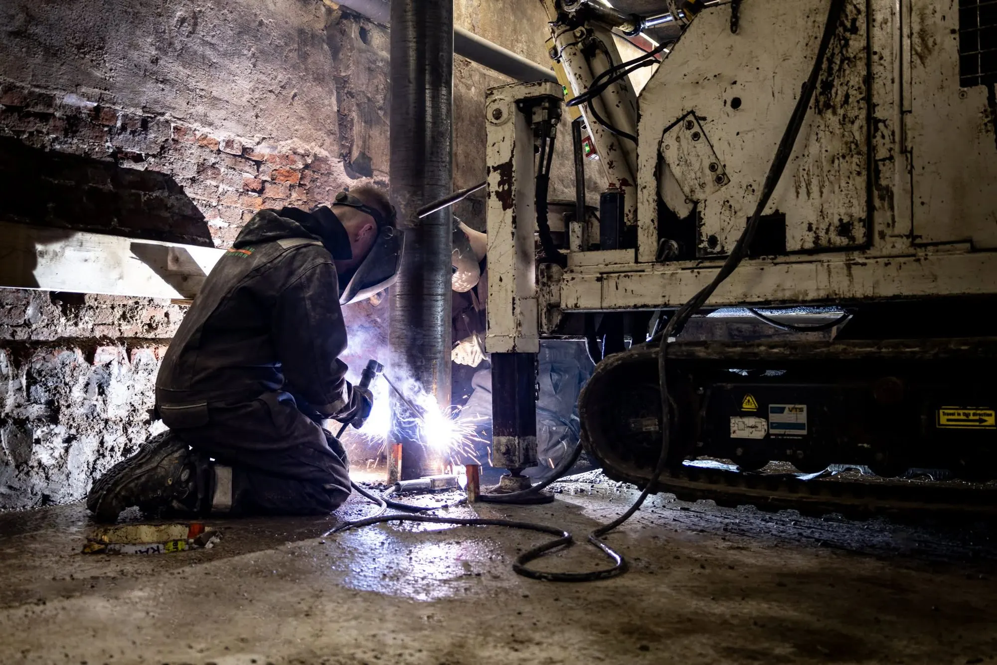 Medewerker last een stalen buispaal onder een gebouw, miniheistelling ernaast