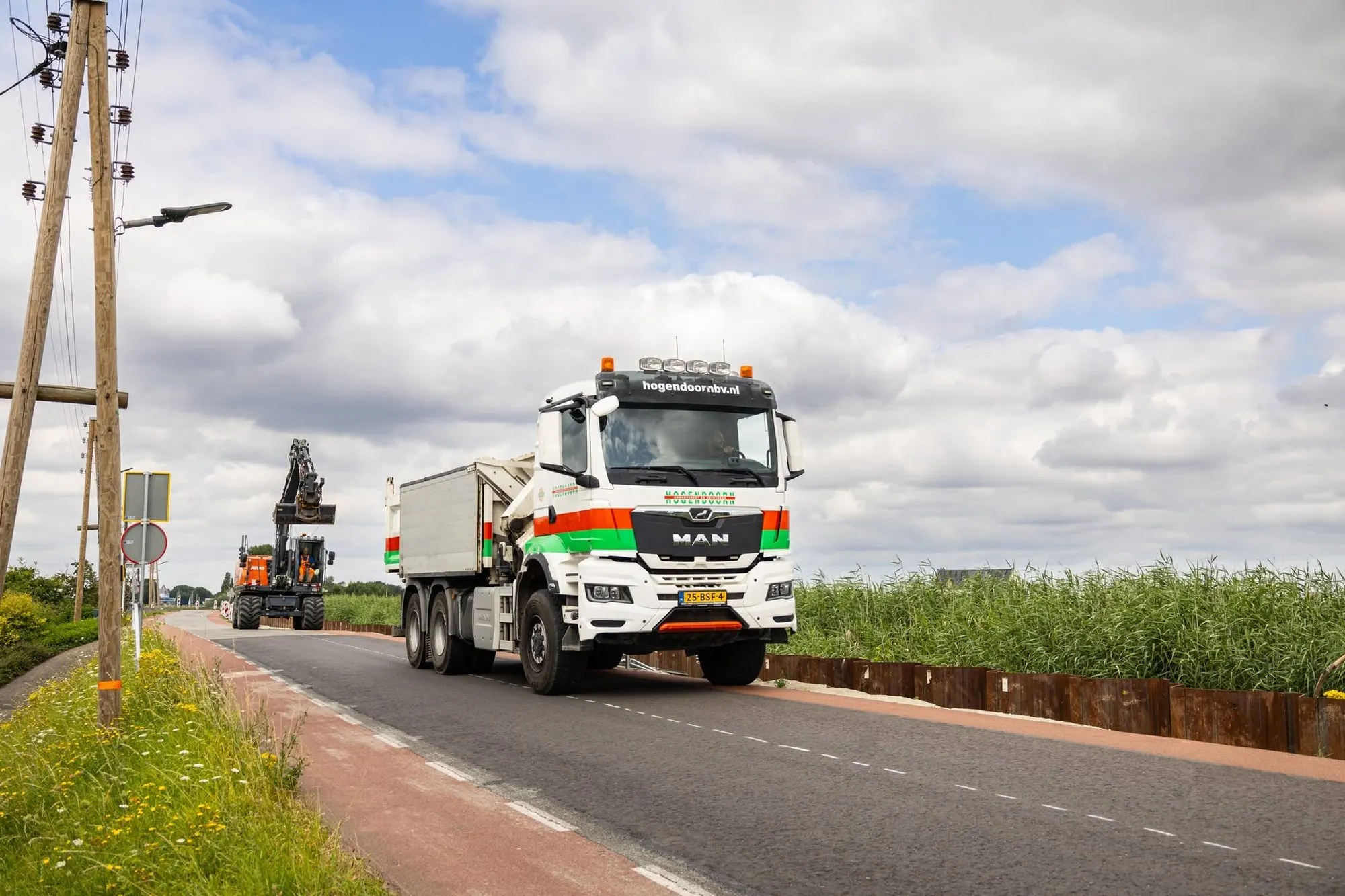 MAN kipper met Hogendoorn-belettering rijdt over een dijkweg, mobiele kraan en damwand op de achtergrond